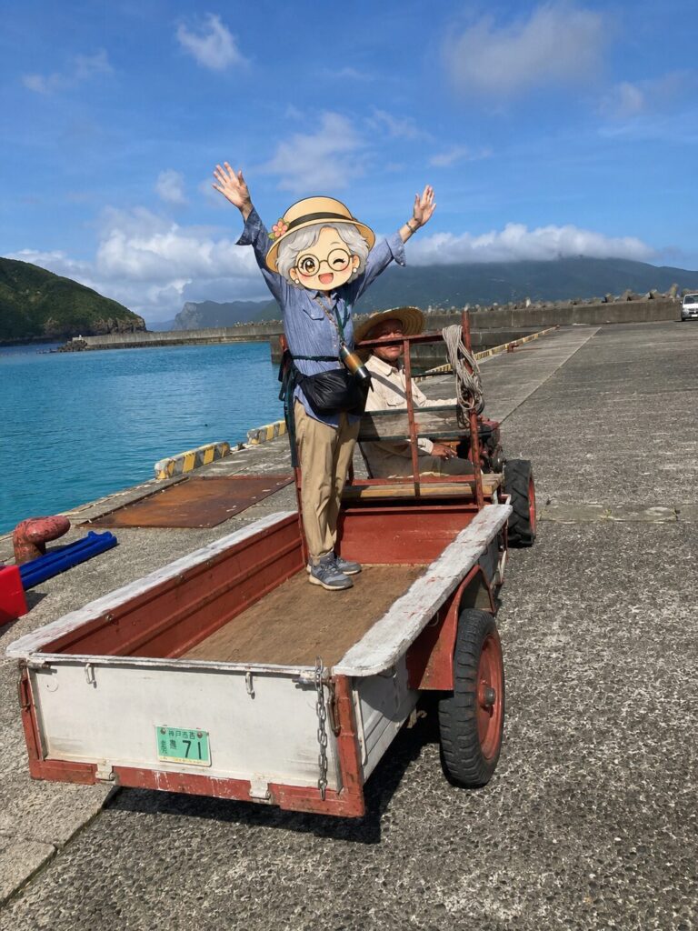 与路島の港で荷物を運んでくれる昔ながらの運搬車。荷台であら古稀キャラクターが万歳しているイラスト合成写真