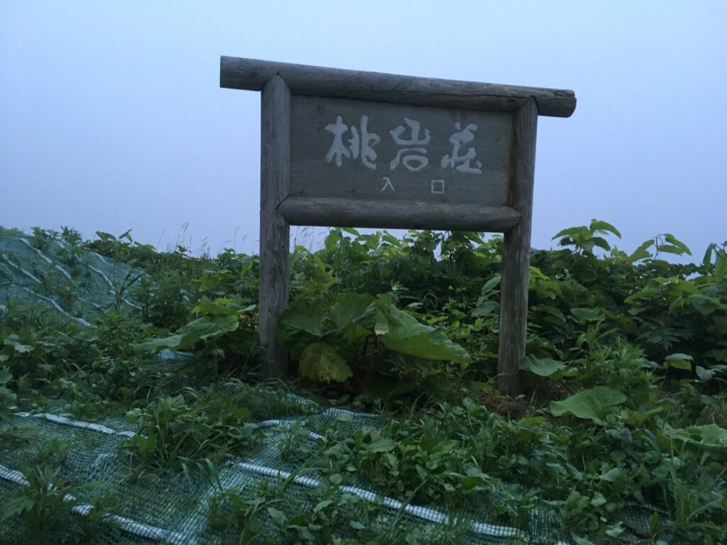 夕暮れに浮かぶ「桃岩荘 入口」の木の看板