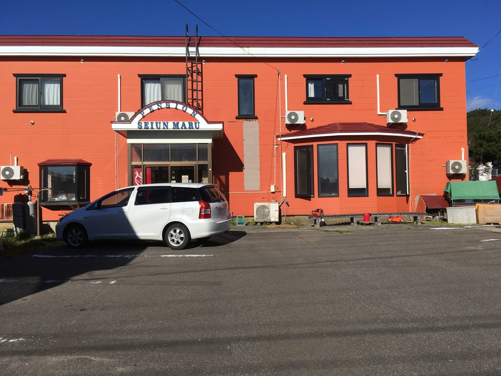 民宿清運丸の外観。オレンジ色の2階建てで「PENSION SEIUN MARU」の看板が掲げられている