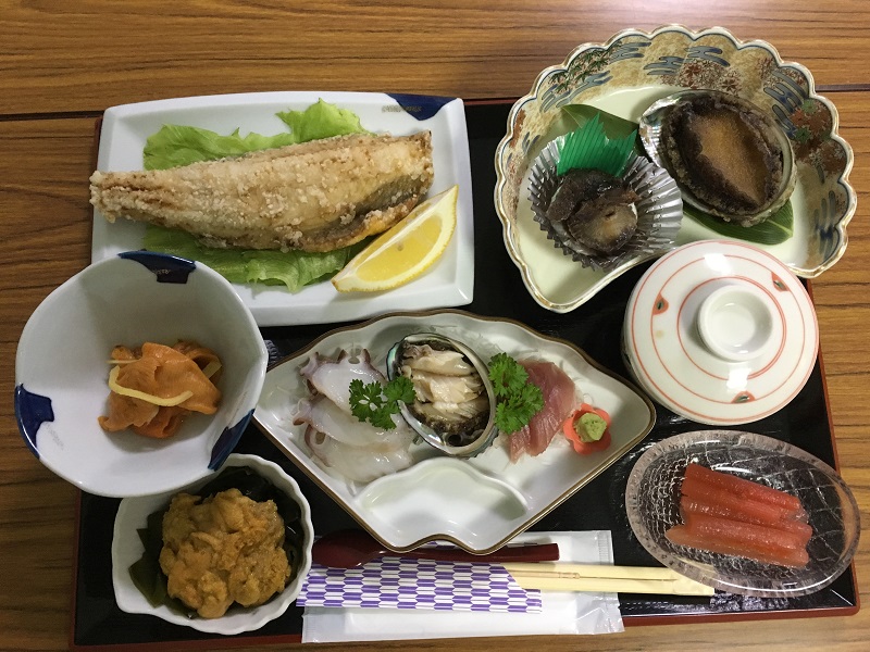 民宿カサイの夕食。生ウニ、殻つきアワビ、刺身の盛り合わせ、焼き魚が並ぶ海の幸のフルコース