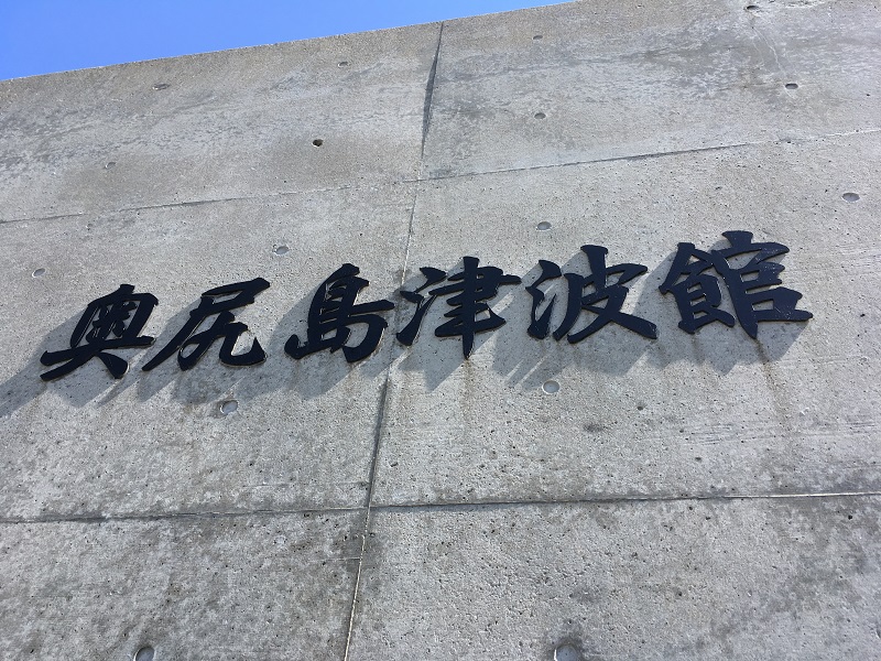 コンクリートの壁に取り付けられた「奥尻島津波館」の切り文字の看板|奥尻島